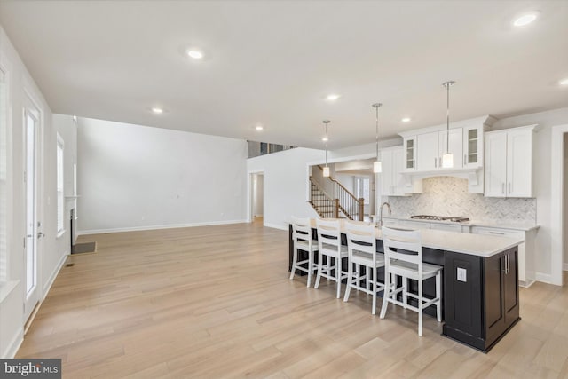 kitchen featuring a breakfast bar, decorative light fixtures, stainless steel gas stovetop, white cabinets, and a center island with sink