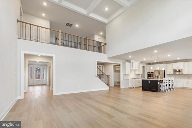 unfurnished living room featuring beam ceiling, a towering ceiling, light hardwood / wood-style flooring, and coffered ceiling