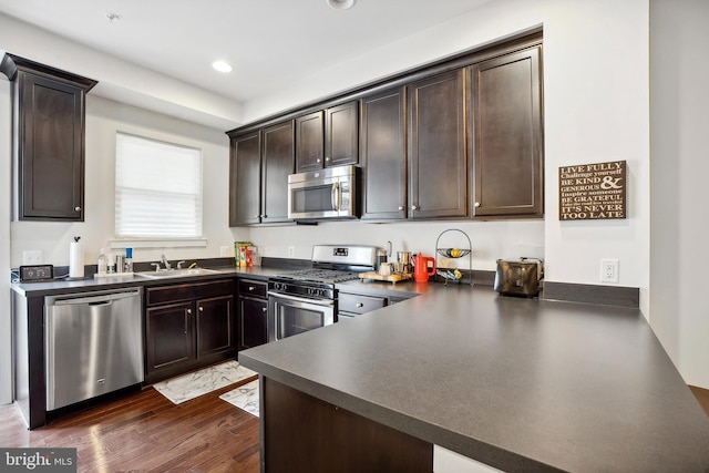 kitchen featuring sink, stainless steel appliances, dark hardwood / wood-style flooring, kitchen peninsula, and dark brown cabinets