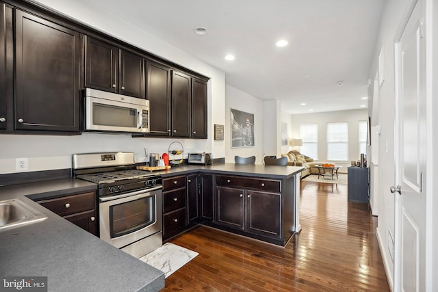 kitchen featuring kitchen peninsula, dark hardwood / wood-style flooring, dark brown cabinetry, and stainless steel appliances