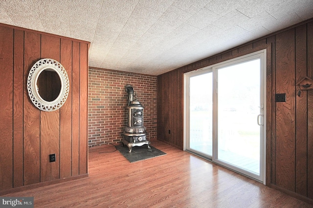 unfurnished living room featuring a wood stove, light hardwood / wood-style flooring, wooden walls, and brick wall