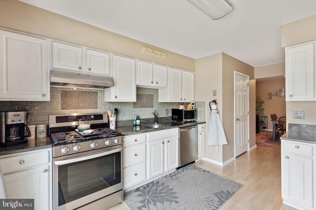 kitchen with appliances with stainless steel finishes, backsplash, sink, light hardwood / wood-style flooring, and white cabinets