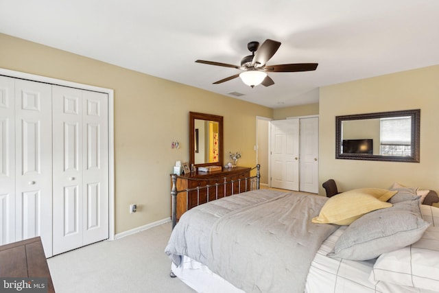 bedroom with ceiling fan, light carpet, and two closets