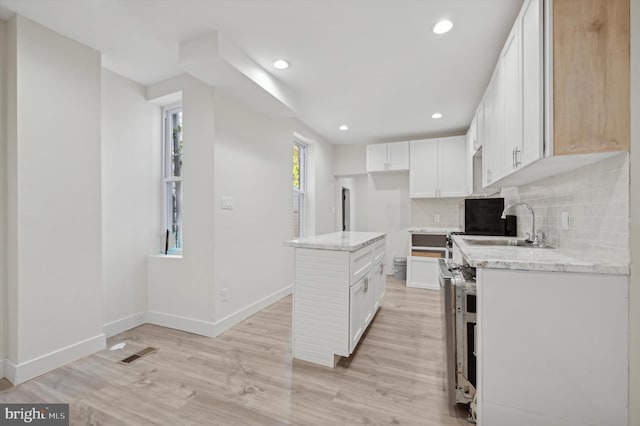 kitchen featuring light stone countertops, a center island, backsplash, light hardwood / wood-style floors, and white cabinets