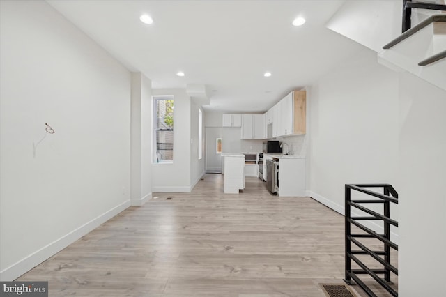 interior space with white cabinets, stainless steel electric range, light hardwood / wood-style floors, and backsplash