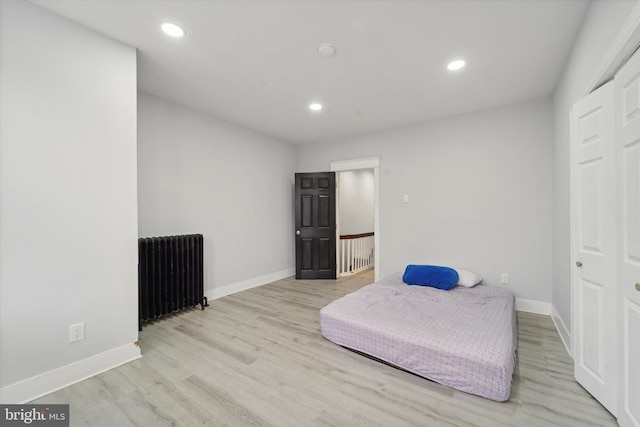 bedroom featuring a closet, radiator heating unit, and light wood-type flooring