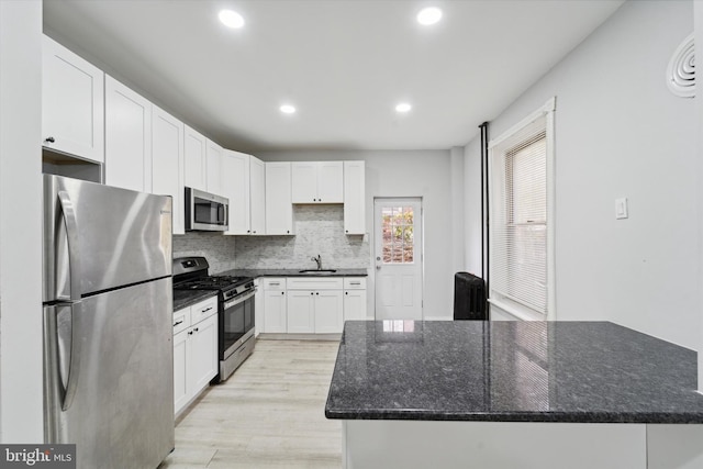 kitchen with light wood-type flooring, stainless steel appliances, sink, dark stone countertops, and white cabinets