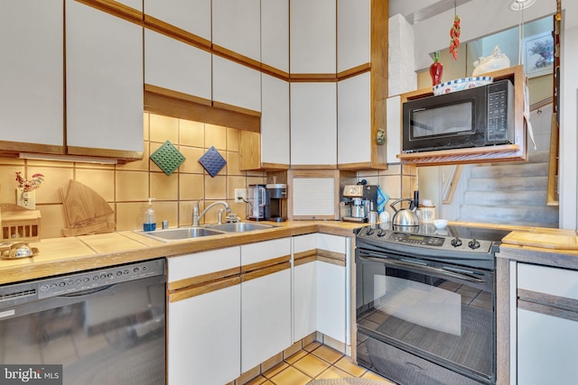 kitchen featuring black appliances, sink, decorative backsplash, light tile patterned floors, and white cabinetry