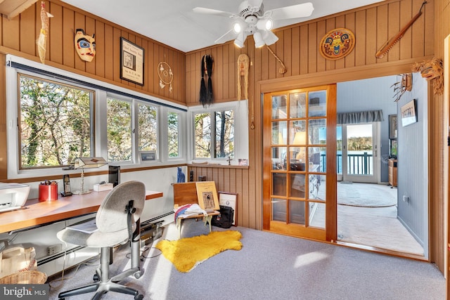 carpeted office space featuring wooden walls, ceiling fan, and a healthy amount of sunlight