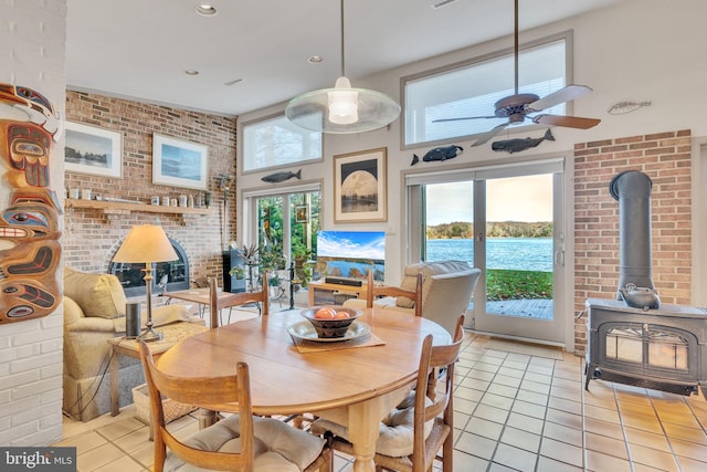 tiled dining room with a healthy amount of sunlight, a water view, a wood stove, and brick wall