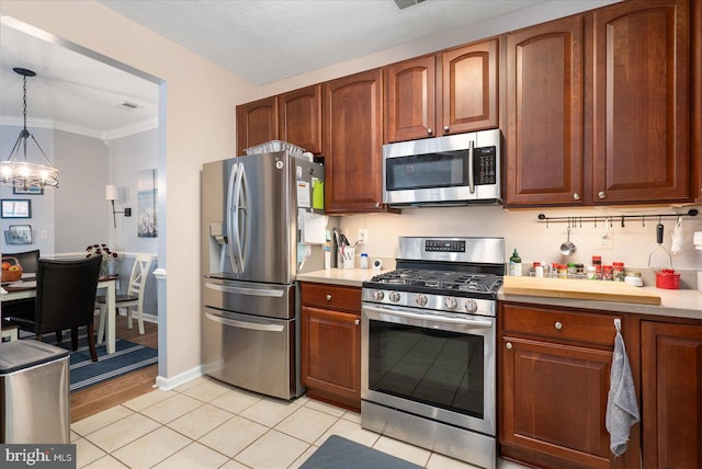 kitchen with light tile patterned flooring, an inviting chandelier, ornamental molding, appliances with stainless steel finishes, and pendant lighting