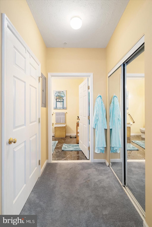 corridor featuring dark colored carpet and a textured ceiling