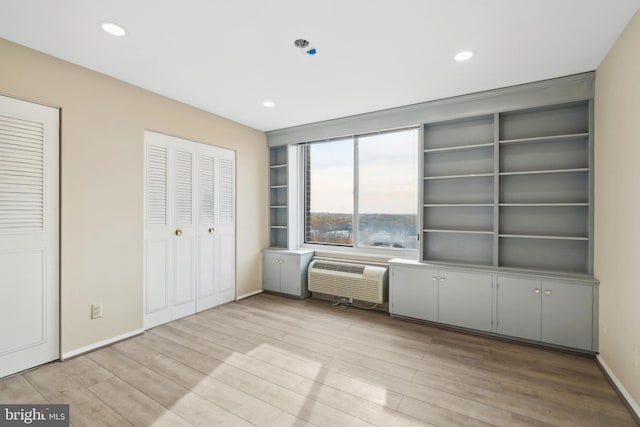 unfurnished bedroom featuring light wood-type flooring, a wall unit AC, and multiple closets