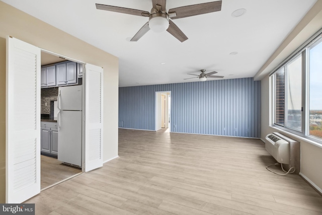 unfurnished living room with a wall mounted air conditioner, light hardwood / wood-style flooring, and ceiling fan