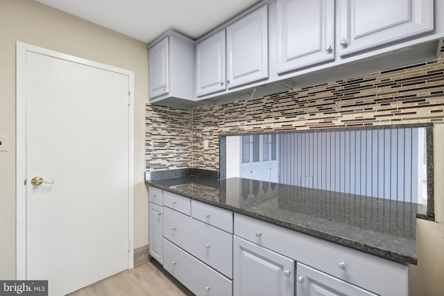 kitchen featuring white cabinets, light hardwood / wood-style floors, dark stone countertops, and tasteful backsplash