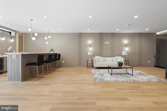 living area featuring beverage cooler, recessed lighting, light wood-style floors, a decorative wall, and indoor wet bar