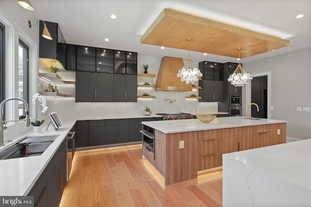 kitchen featuring premium range hood, a kitchen island with sink, sink, decorative light fixtures, and an inviting chandelier