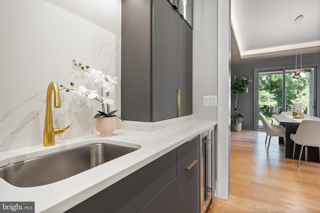 kitchen featuring pendant lighting, sink, wine cooler, light wood-type flooring, and light stone counters