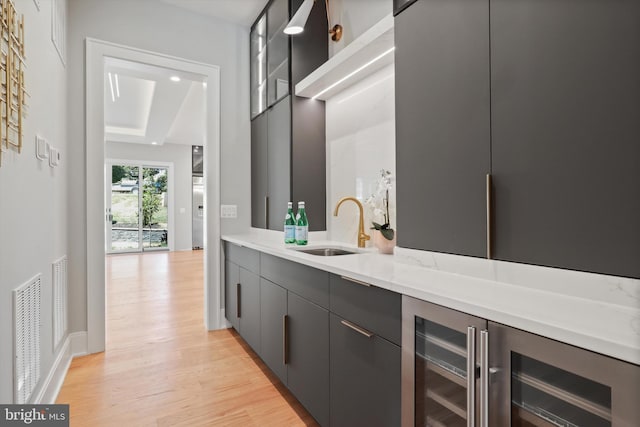 bar featuring baseboards, visible vents, light wood finished floors, a sink, and wine cooler