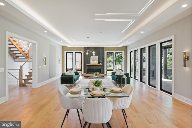 dining room with a tray ceiling, a healthy amount of sunlight, stairs, and light wood finished floors