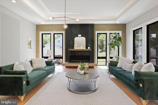 living room with a raised ceiling, a fireplace, wood-type flooring, and a notable chandelier