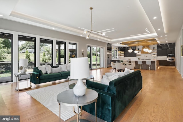 living room with a raised ceiling, light wood-type flooring, and an inviting chandelier