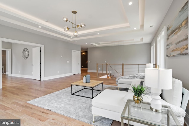 living area featuring a notable chandelier, light wood-style flooring, baseboards, and a tray ceiling