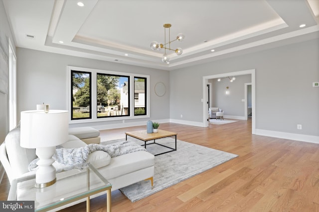 living area featuring an inviting chandelier, a tray ceiling, baseboards, and light wood-type flooring