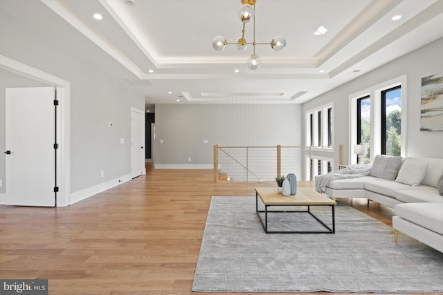 living area featuring an inviting chandelier, a tray ceiling, light wood-style flooring, and baseboards