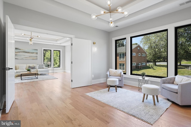 living area with a tray ceiling, plenty of natural light, an inviting chandelier, and light hardwood / wood-style flooring