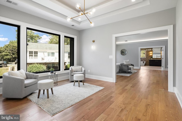 living area featuring an inviting chandelier, light hardwood / wood-style floors, and a raised ceiling