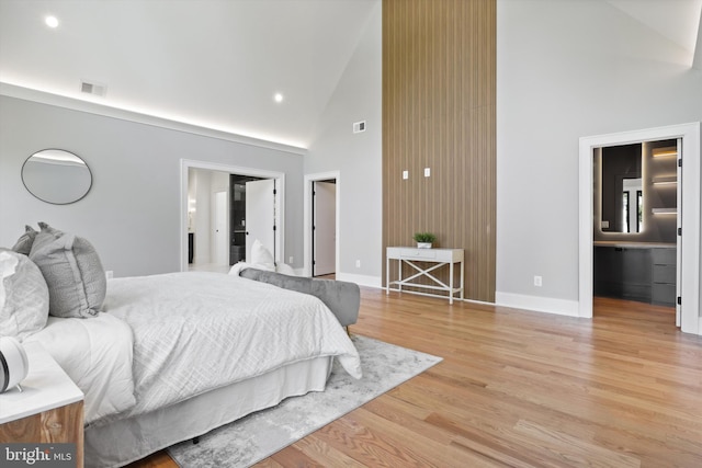 bedroom with ensuite bathroom, high vaulted ceiling, and light wood-type flooring