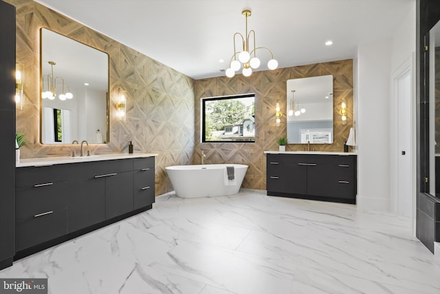 bathroom with a notable chandelier, marble finish floor, a freestanding bath, and two vanities