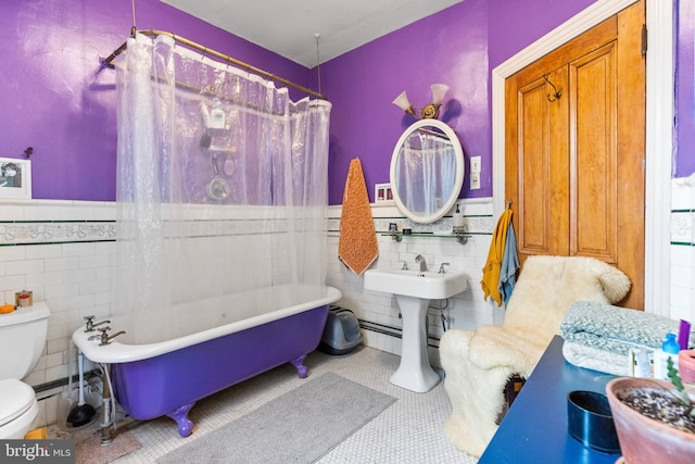 full bathroom featuring a wainscoted wall, tile walls, a freestanding bath, toilet, and tile patterned floors