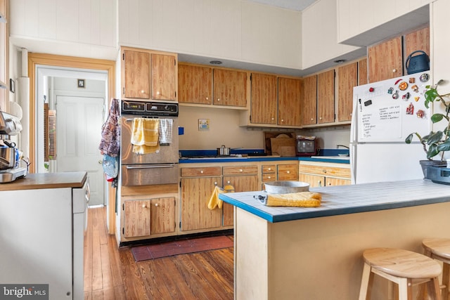 kitchen featuring brown cabinetry, dark wood-style floors, appliances with stainless steel finishes, a peninsula, and a warming drawer