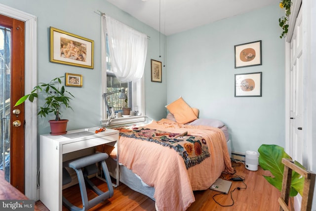 bedroom with multiple windows, baseboard heating, and wood finished floors