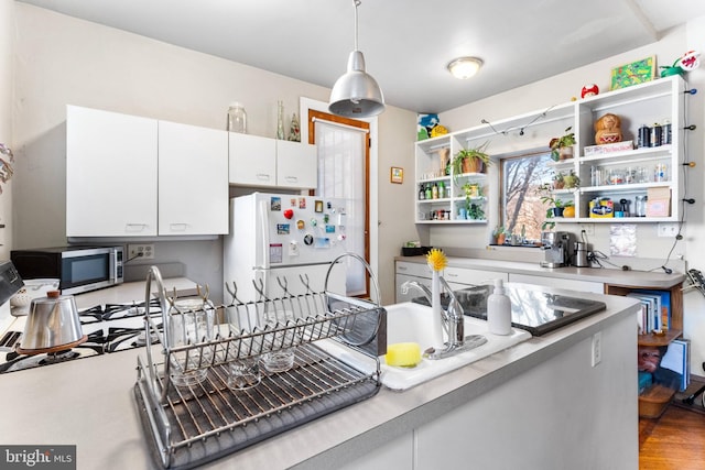 kitchen with open shelves, light countertops, stainless steel microwave, freestanding refrigerator, and white cabinets