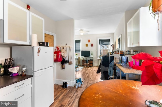 kitchen featuring a ceiling fan, freestanding refrigerator, glass insert cabinets, white cabinetry, and wood finished floors