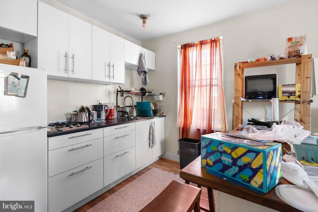 kitchen featuring dark countertops, freestanding refrigerator, white cabinets, a sink, and light wood-type flooring