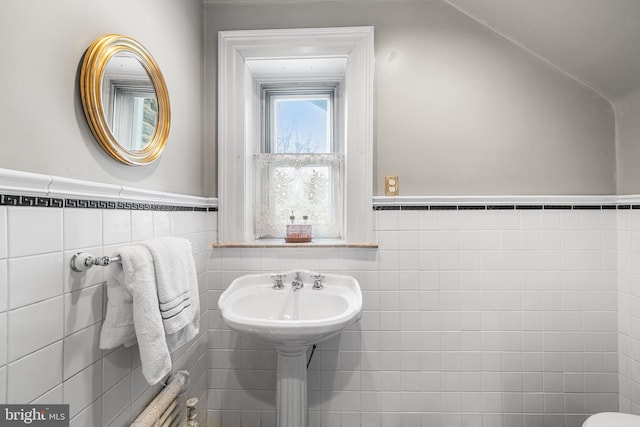 half bath featuring a sink, a wainscoted wall, and tile walls