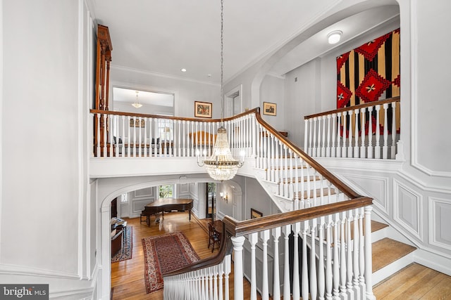 staircase featuring arched walkways, wood finished floors, crown molding, and a notable chandelier