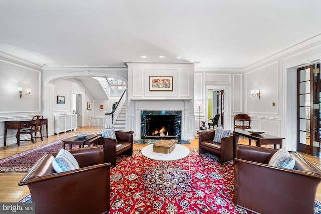 living room featuring a decorative wall, a fireplace, arched walkways, stairway, and wood finished floors