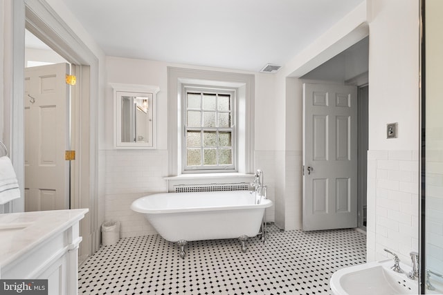 bathroom with a soaking tub, a bidet, visible vents, and tile walls
