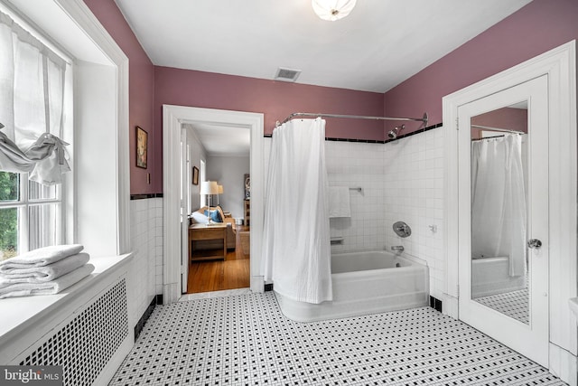 bathroom featuring shower / bathtub combination with curtain, vanity, radiator heating unit, visible vents, and tile walls