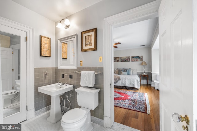 bathroom with tile walls, toilet, a ceiling fan, wood finished floors, and a wainscoted wall