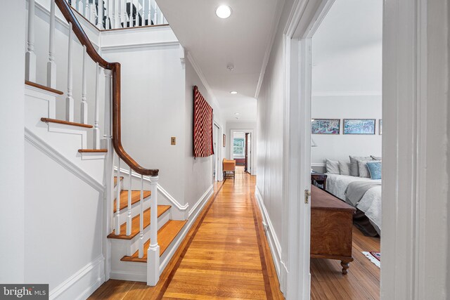hallway with ornamental molding, baseboards, light wood-type flooring, and stairway