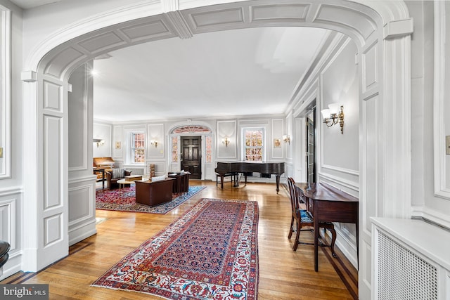hallway featuring arched walkways, a decorative wall, wood-type flooring, and radiator