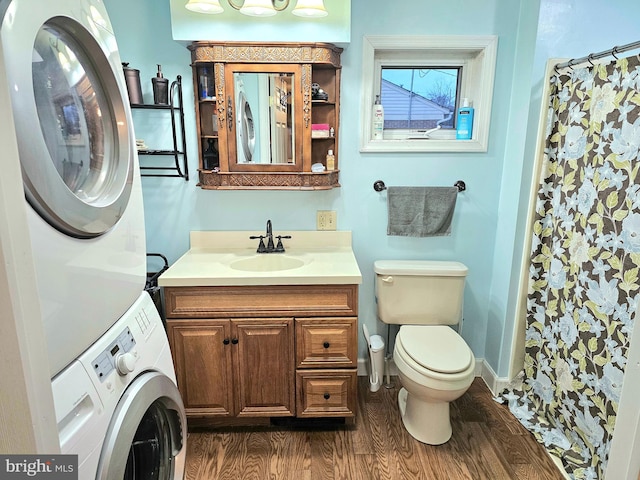 bathroom with hardwood / wood-style floors, vanity, toilet, stacked washing maching and dryer, and walk in shower