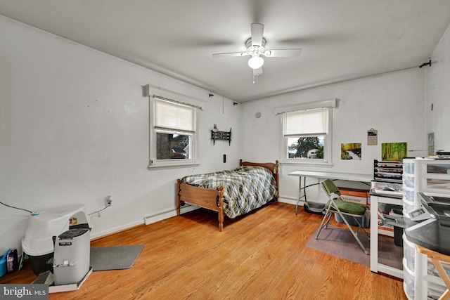 bedroom featuring baseboard heating, light hardwood / wood-style flooring, and ceiling fan