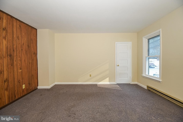 unfurnished room featuring dark colored carpet, wood walls, and a baseboard radiator